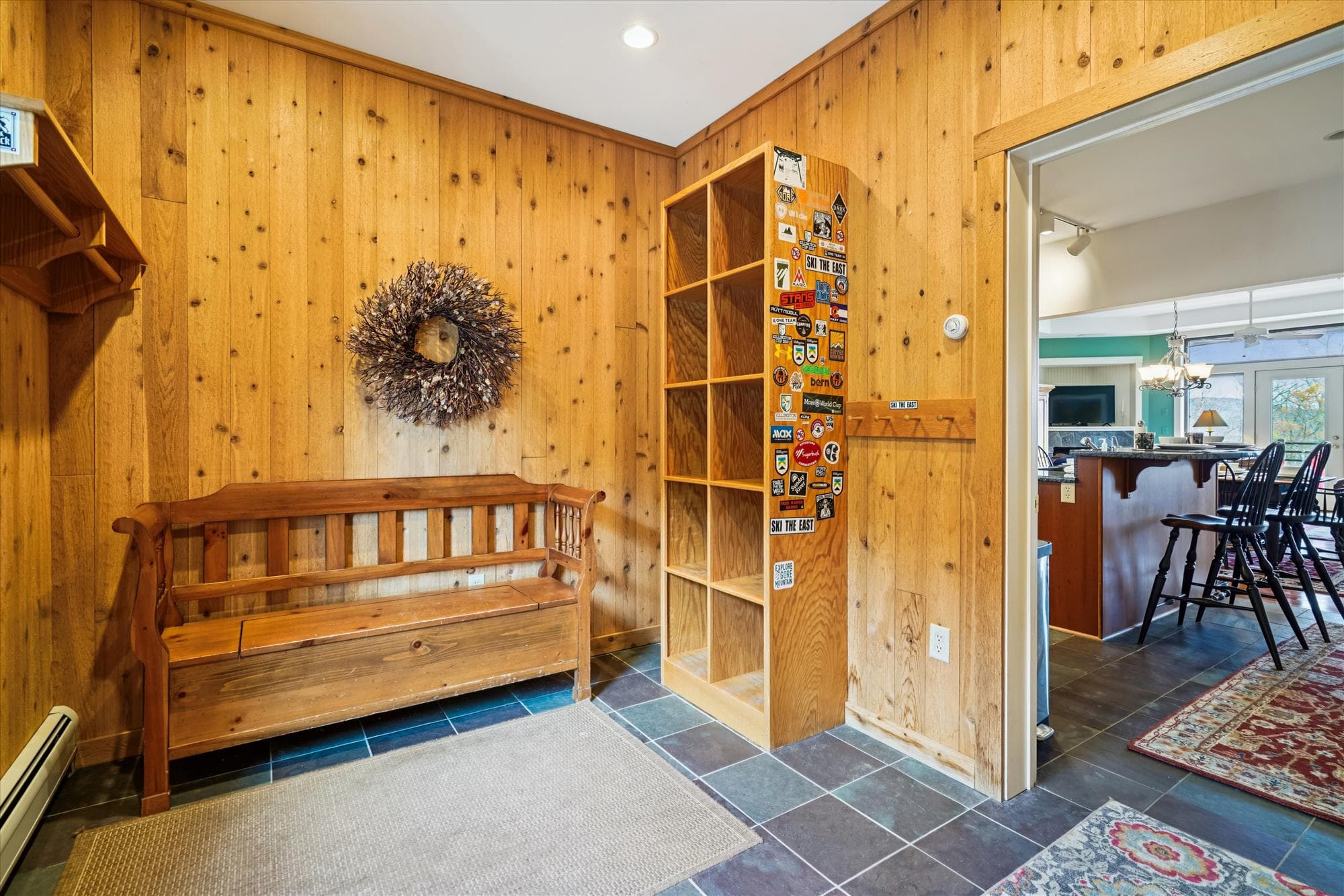 Inviting lodge entrance with slate tile floors, classic wood paneling, a storage bench, and decorative snowshoes. Functional and charming space for winter gear before entering the main living area.