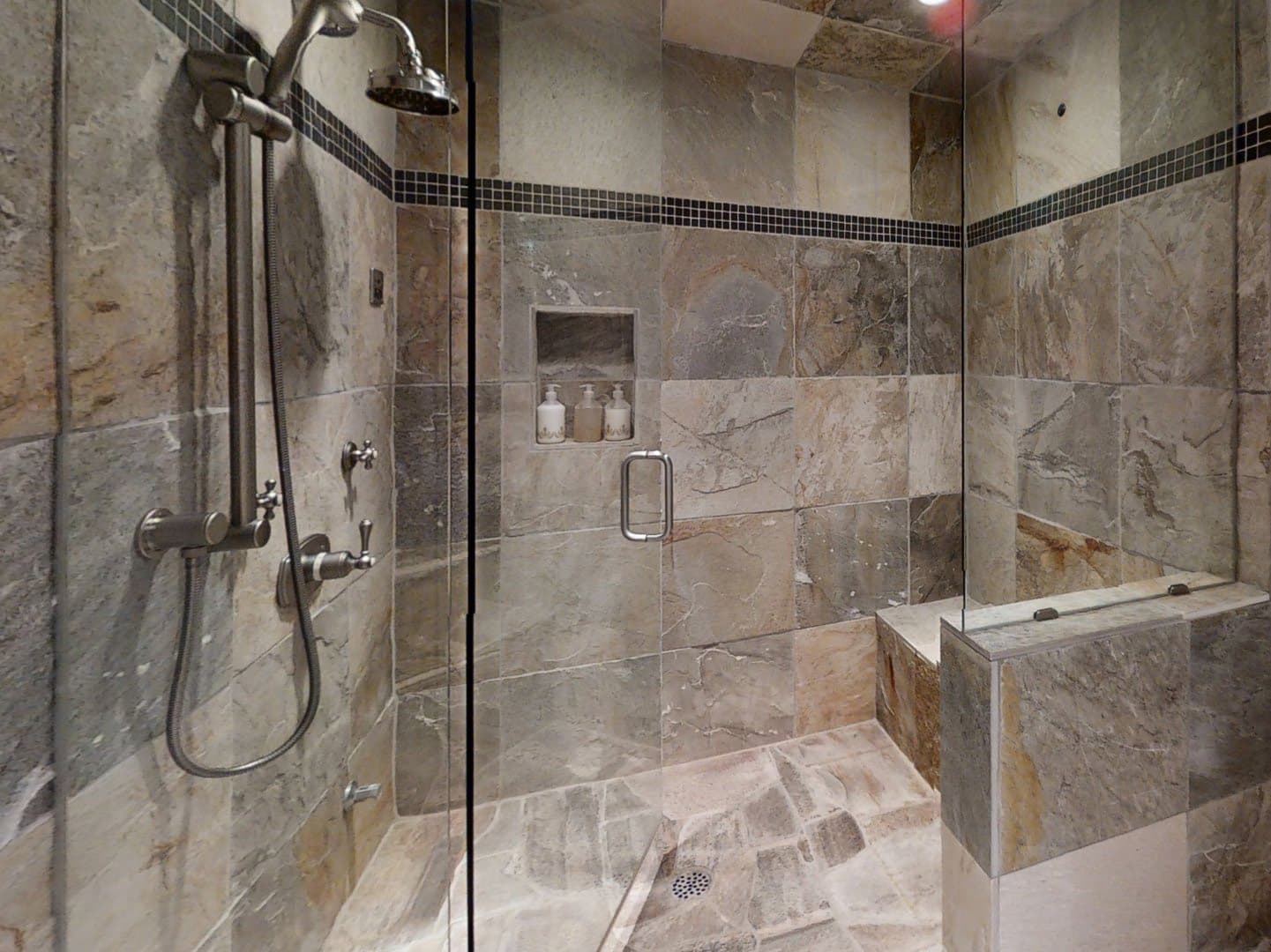 A close view of the home's steam shower, with tile covered walls, a movable showerhead, and a walk-in design.