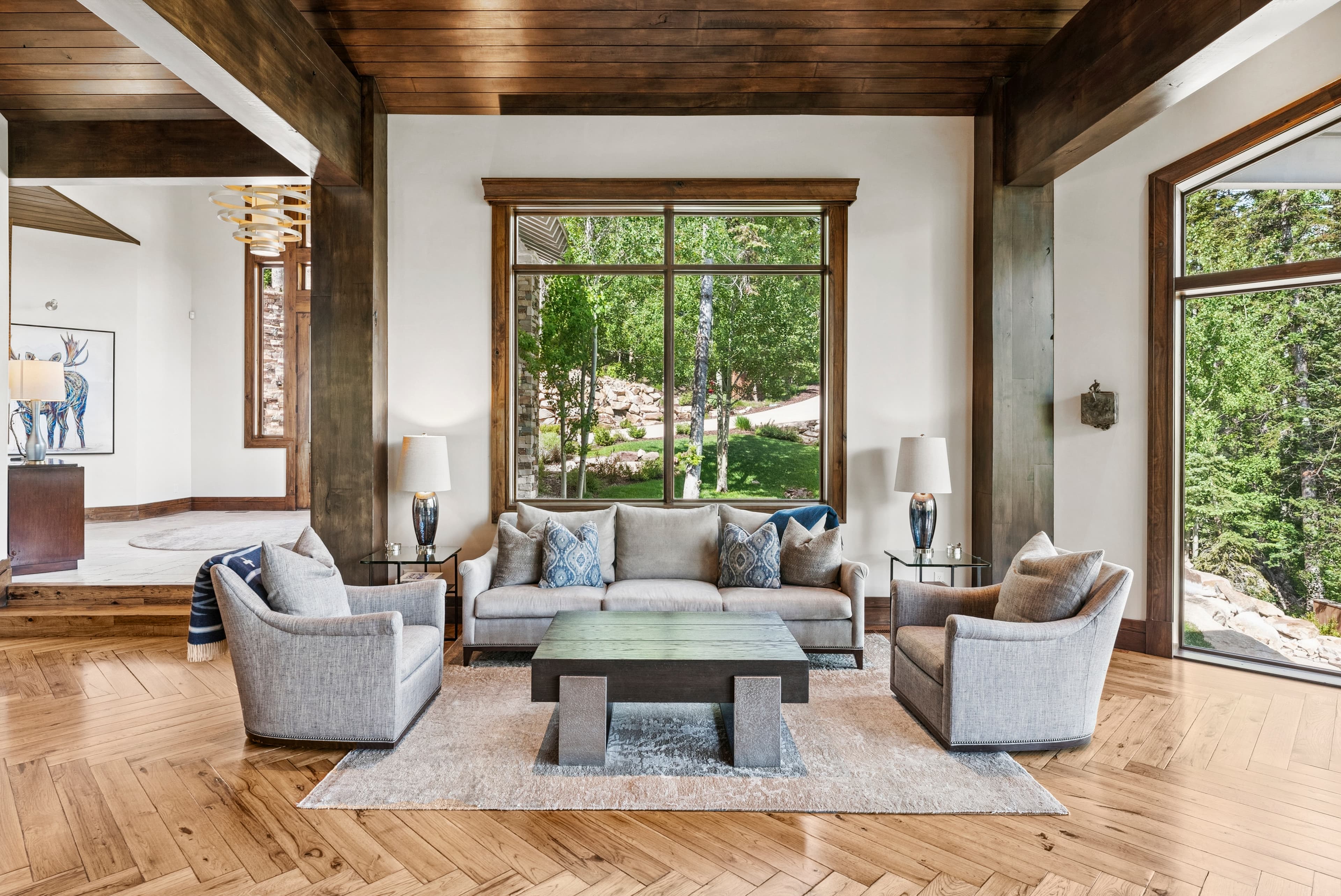 a cozy gathering area with overstuff couches, designer accents and large windows with forest views