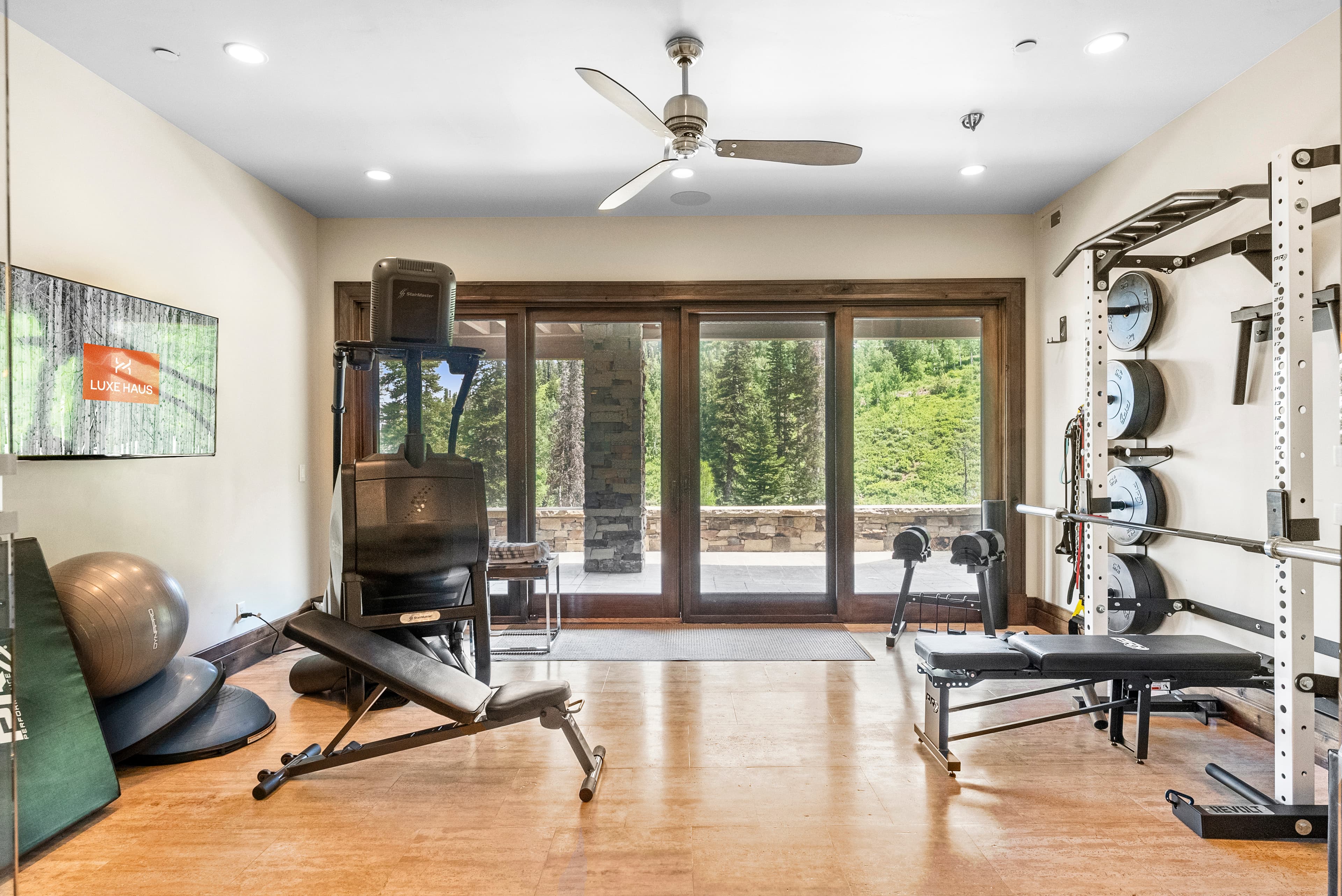 the gym at grandview with workout equipment, weight machines and a large TV with the Luxe Haus logo on it. there is a large door that leads out to the deck
